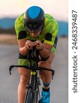  Close up photo of triathlete riding his bicycle during sunset, preparing for a marathon. The warm colors of the sky provide a beautiful backdrop for his determined and focused effort.