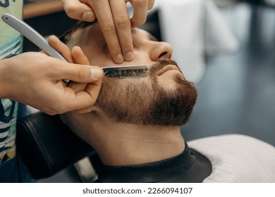 close up photo  of trimming a man's beard with a dangerous razor. A barber cuts a beard in a barbershop. Beard trimming in a beauty salon for men - Powered by Shutterstock