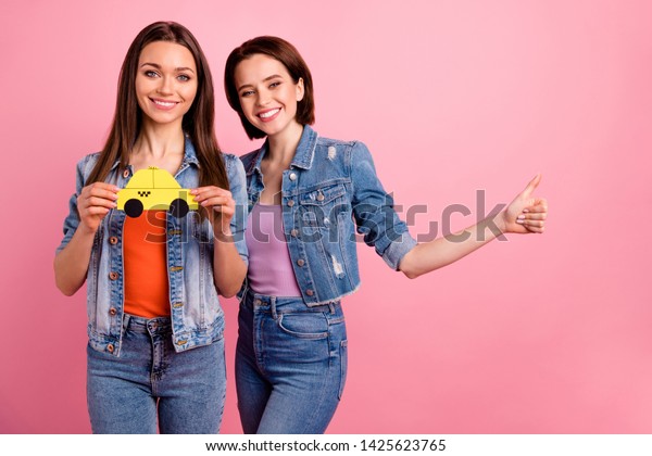 Close up photo two beautiful she her sisters\
ladies buddies hands arms paper advert yellow taxi users thumb up\
symbol tips advising wear jeans denim jackets blazers isolated\
bright pink background