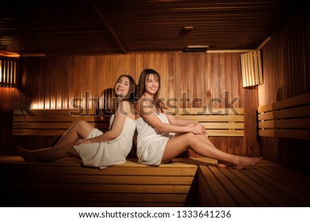 close up photo of two beautiful women wearing white towels in a wooden sauna