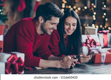 Close up photo of two romantic people  lying on floor with gift boxes using device looking blogs enjoy noel x-mas holidays christmas party  in house full of newyear lights indoors