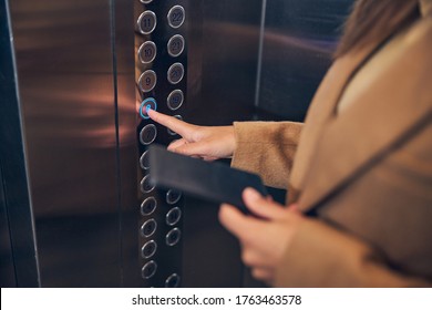 Close up photo of woman in brown coat pressing button of the lift to go down - Powered by Shutterstock