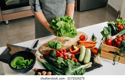 Close Up Photo of Woman Hands Holding Fresh Lettuce while Standing at Kitchen Table Full with Fresh Vegetables for Salad Bowl