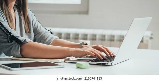 Close up photo of woman hands typing business report on a laptop keyboard at the kitchen desk with a digital tablet, notebook and wireless earphones