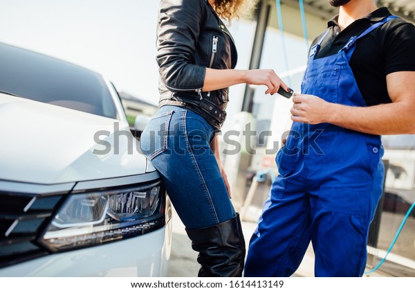 Close up\
photo,  woman stands with a man in blue uniform who washes cars at\
the self-service sink and gives him the\
keys.