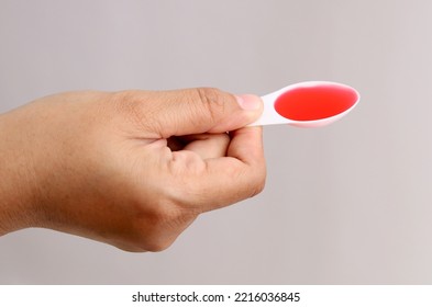 Close Up Photo Of Woman's Hand Holding A Spoon Of Syrup Medicine. Isolated On Gray Background