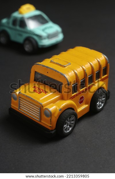 close\
up photo of a yellow school bus toy on asphalt with blurred taxi\
toy background. school bus miniature for kids\
play