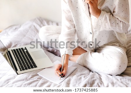 Close up photo of young beatiful girl is talking by phone and writes a note. Home office. Concept of working and studying at isolation.