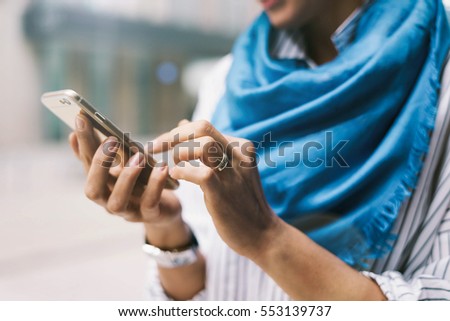 Close up photo of young girl reading messages on a smartphone while standing on urban background. Electronic device in the hands of hipster girl who is posting tweets  by using mobile application.