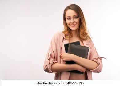 Close Up Photo Of Young Pretty Long Haired University Teacher, Dressed In Pink Romantic Clothes, Holding File Folder And Ipad In Her Hands, Looking A Bit Down With Beautiful Embarrassed Smile.