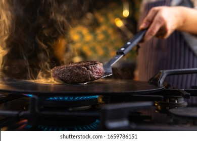 Close up photograph of a female chef flipping a tasty, juicy burger on a hot kitchen stove - Powered by Shutterstock