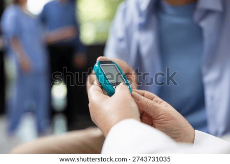 Close up of physician using digital glucometer to measure blood sugar levels in hospital lobby. Professional doctor uses glucose monitor and test strip for routine blood sugar testing on patient.