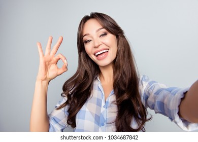 Close up picture of pretty, attractive, nice, cute woman with beaming smile shooting selfie, gesturing ok sign with fingers, having video call, standing over grey background