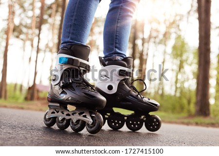 Close up picture of rollerblades, unknown person wearing rollerskates to spend time actively, black rollerblades with wheels being on road in fresh air, trying new purchase. Rollerskating concept.
