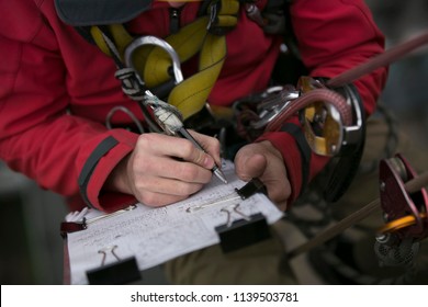 Close Up Picture Of Rope Access Technician Engineer Worker Writing A Report Of Building Structure Leak, Hiatus At Hight Rise Construction Building Site Sydney, City Skyline, Australia      
