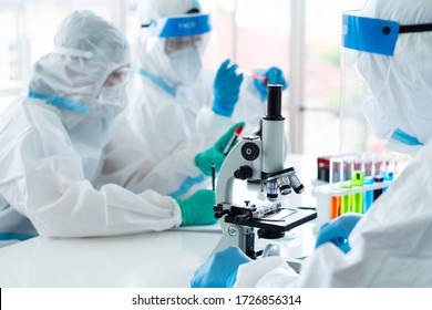 Close Up Picture Of Scientist Wearing Personal Protective Equipment Or Ppe Using Microscope To Do Experiment About Covid-19 Or Coronavirus Vaccine In The Lab. Science And Medical Concept