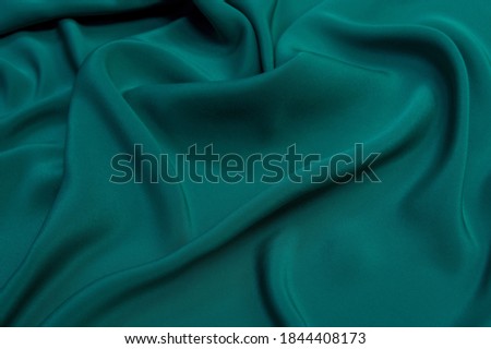 Close up picture of silk satin fabric with wavy holds in emerald color. Textured background of soft satin for design. 
