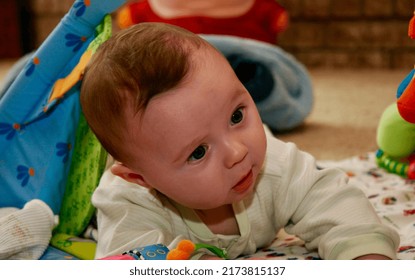 Close Up Picture Of A Sweet Baby Boy Laying On His Tummy While Holding His Head Up.   He Has Brown Hair, Blue Eyes, And Baby Soft Skin.