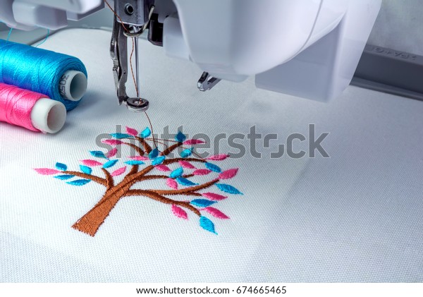 Close\
up picture workspace of  embroidery machine \
show embroider tree\
design theme. And two thread s cyan and pink\
color.