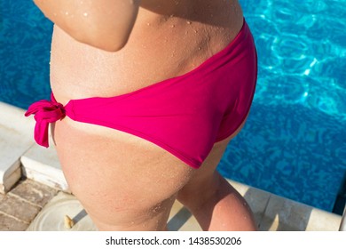 Close up picture of a young female buttock wearing pink swimsuit, pool in the background
