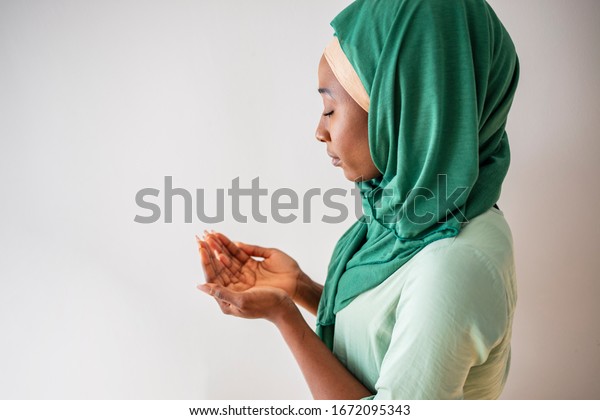 Close up picture of\
a young muslim woman praying. Young Muslim woman Praying with\
folded hands. She has a green veil covering her head. Young muslim\
woman praying in mosque
