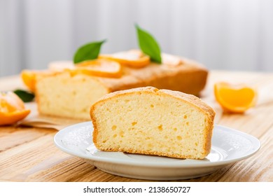 Close up piece of moist orange fruit pound cake on plate with slices of orange and whole pie on background. Delicious breakfast, traditional English tea time. Recipe of orange pie loaf.