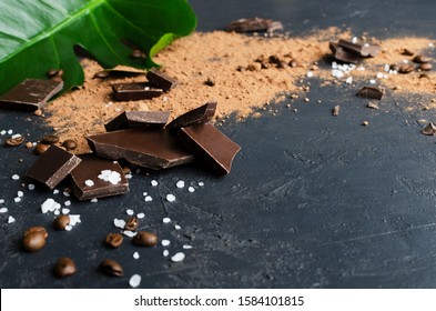 Close up of pieces of dark chocolate, salt, cocoa powder, coffee beans on the dark sufce.Concept of natural salty chocolate.Empty space for design