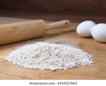 A close up of a pile of flour along with eggs and a rolling pin on a wooden cutting board. - Powered by Shutterstock