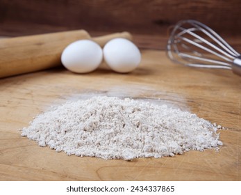 A close up of a pile of flour along with eggs and a rolling pin on a wooden cutting board. - Powered by Shutterstock