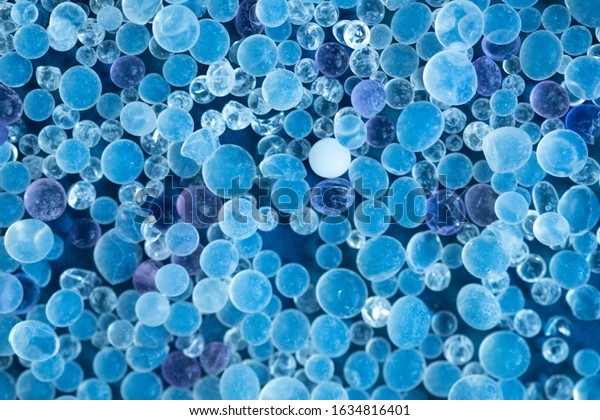 Close up - Pile of silica gel on blue background,\
Desiccant used in industrial, moisture protection. Desiccant Silica\
Gel (Moisture Absorber) Background. Blue and White Translucent\
Crystals Texture