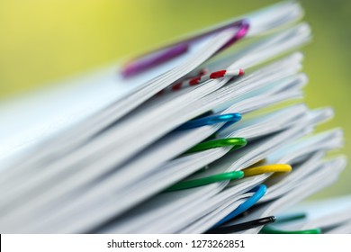 Close up pile of unfinished homework assignment stacked in archive with colorful paper clips on table in school waiting to be managed and inspected. Stack of paperwork. Education and business concept.