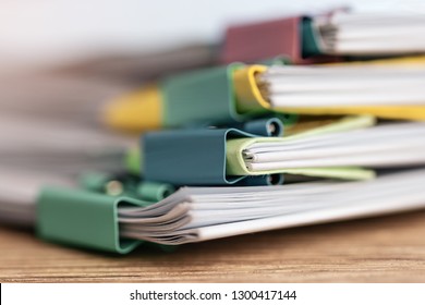 Close up pile of unfinished paperwork on office desk waiting to be managed and inspected. Stack of homework assignment with colorful paper clips. Report papers stacks. Business and education concept. - Shutterstock ID 1300417144