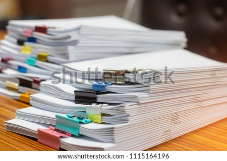 Close up pile of unfinished paperwork on office desk waiting to be managed. Stack of homework assignment with paperclips. Report papers stacks. Business and education concept.