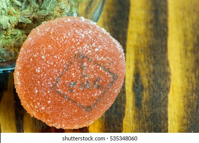 Close Up Of Pink Cannabis Edible In Front Of A Jar Of Marijuana Bud On A Wooden Background