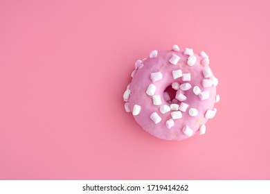 A close up of a pink donut with marshmallow on pink paper background. Top view with copy space.