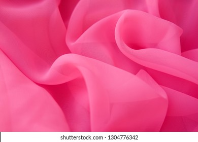 Close up pink silk fabric. The pink fabric is laid out waves. Purple sateen fabric for background or texture.  