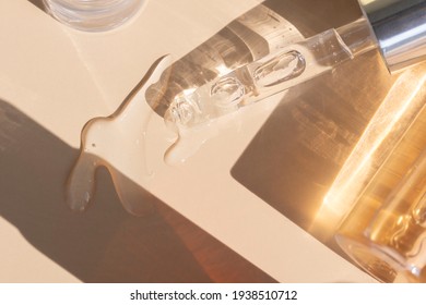 Close Up Of Pipette With Pouring Liquid Serum With Golden Bottle And Shadows On Beige Background