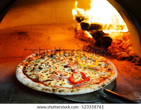 Close up pizza in firewood oven with flame behind