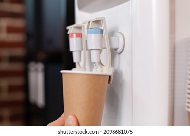 Close Up Of Plastic Cup On Water Cooler For Refreshment In Business Office. Hot And Cold Faucet With Purified Water Beverage In Indoors Space. Water Dispenser Appliance With Tap.