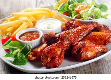 Close Up Plate For Main Entree With Crispy Fried Chicken Drumsticks Paired With Potato Fries, Veggies And Homemade Gravy, Served On Wooden Table.