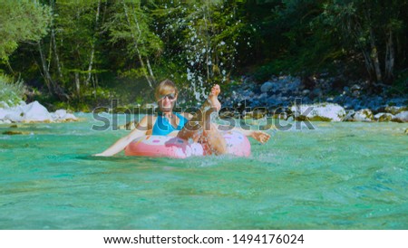 CLOSE UP Playful woman splashing water while floating downstream on doughnut-shaped floatie. Cheerful girl enjoying her riverside vacation on sunlit day. Female having fun time on floatie.