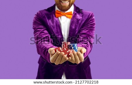 Close up of poker chips in hands of joyful excited man isolated on purple background. Cropped image of man in velvet purple jacket smiling. Casino, gambling, poker, people and entertainment concept.