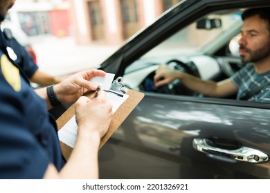 Close up of a police cop writing a traffic ticket or fine to a male driver in his car for speeding