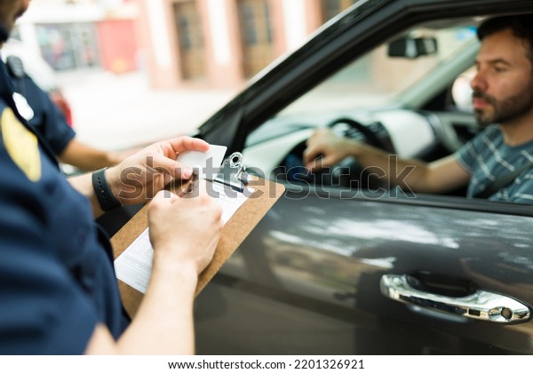 Close up of a police cop\
writing a traffic ticket or fine to a male driver in his car for\
speeding