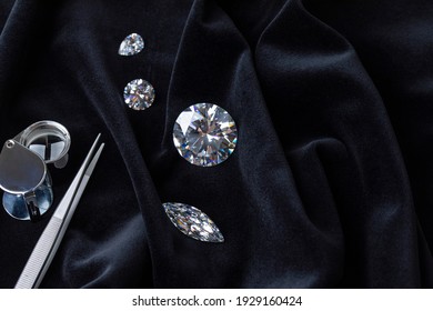 Close up of polished diamonds different cuts and sizes with tweezers and magnifying glass on black velvet fabric top view with copy space. - Shutterstock ID 1929160424