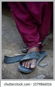 Close Up Of A Poor Child On The Street With Dirty Broken Slippers, Muddy Feet & Torn Rugged Clothes. Child Labor And Slavery Depicted In A Picture. Devastating Condition Of Children Around The World