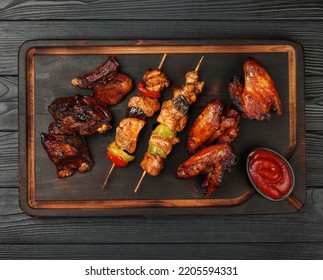 Close Up Portion Of Mixed Grilled Barbecue Combo Plate With Chicken Buffalo Wings, Beef Spare Ribs And Skewer Meat On Wooden Board Over Black Table Planks, Elevated Top View, Directly Above