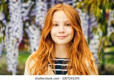 Close up portrait of adorable 9-10 year old red-haired kid girl posing in wisteria