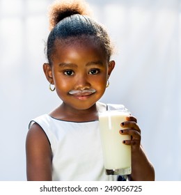 Close up portrait of adorable little African girl drinking glass of milk.Isolated against light background.