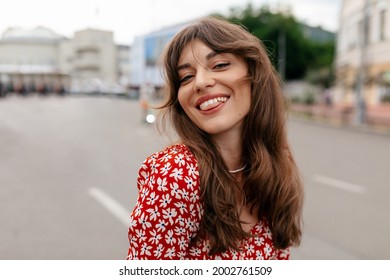 Close up portrait of adorable smiling elegant woman in summer dress posing at camera while walking in the city